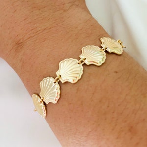 May include: A gold bracelet with a chain and five shell-shaped charms. The bracelet is on a person's wrist.