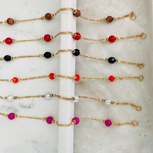 May include: Six gold chain bracelets with different colored beads. The bracelets feature red, black, orange, white, and pink beads.