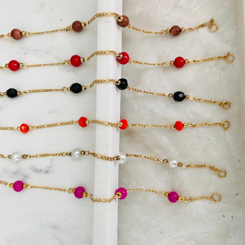 May include: Six gold chain bracelets with different colored beads. The bracelets feature red, black, orange, white, and pink beads.
