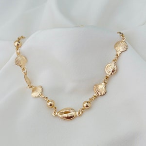 Könnte beinhalten: Eine goldene Halskette mit einer zarten Kette und Muschel-Anhängern. Die Halskette liegt auf einem weißen Hintergrund.