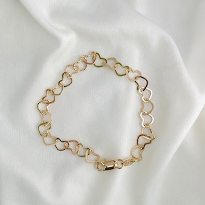 Puede incluir: Un brazalete de cadena de oro en forma de coraz&oacute;n. El brazalete est&aacute; hecho de peque&ntilde;os eslabones en forma de coraz&oacute;n interconectados.