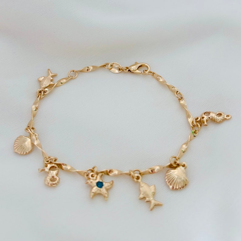 May include: A gold charm bracelet with a twisted chain and various sea-themed charms, including a starfish, seashells, and fish.