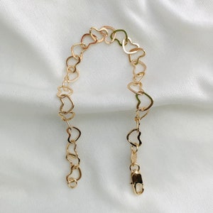 Puede incluir: Un brazalete de cadena de oro en forma de coraz&oacute;n. El brazalete est&aacute; hecho de eslabones entrelazados en forma de coraz&oacute;n.
