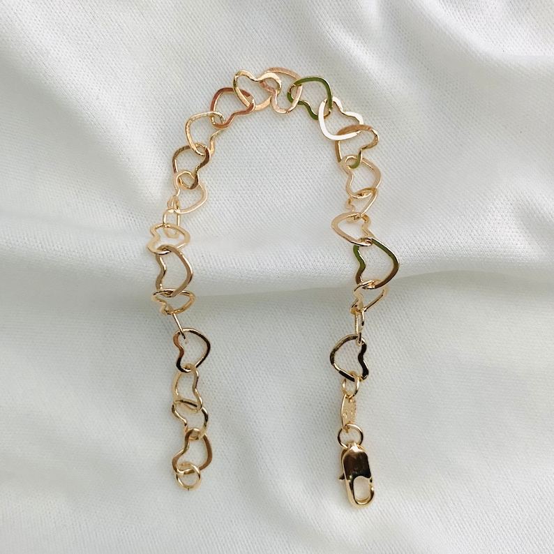 Puede incluir: Un brazalete de cadena de oro en forma de coraz&oacute;n. El brazalete est&aacute; hecho de eslabones entrelazados en forma de coraz&oacute;n.