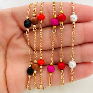 May include: Five gold chains with different colored beads. The beads are red, orange, pink, brown, black, and white.