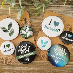 May include: Assortment of round buttons with various designs.  Some buttons feature a green leaf design, while others have a heart with the text "I ♥ Herbalife".  Two buttons feature the text "Lose Weight Now Ask Me How!" with a black and green design and a blue and green design.