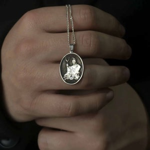 May include: A silver chain necklace with an oval pendant featuring a detailed engraving of a mythical creature holding a trident.