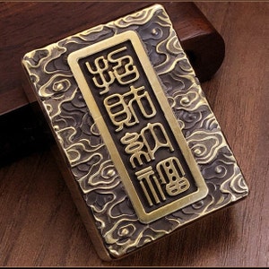May include: A rectangular, antique-style lighter with a brass finish. The lighter features an embossed cloud pattern and a rectangular brass plate with Chinese characters. The overall design is detailed and ornate.