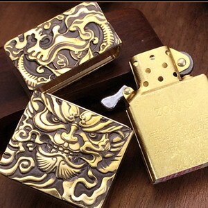 May include: A gold-colored ZORRO lighter with intricate dragon and demon face designs. The lighter's case features detailed relief carvings. The open lighter reveals the internal mechanism. The text "ZORRO" is visible on the lighter.