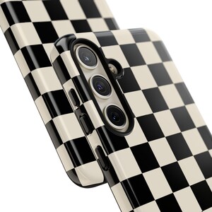 May include: Close-up of two phone cases with a black and cream checkerboard pattern. The phone case on top has a camera module with three lenses. The cases have a glossy finish and a modern design.
