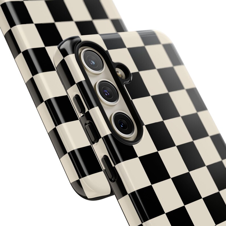 May include: Close-up of two phone cases with a black and cream checkerboard pattern. The phone case on top has a camera module with three lenses. The cases have a glossy finish and a modern design.