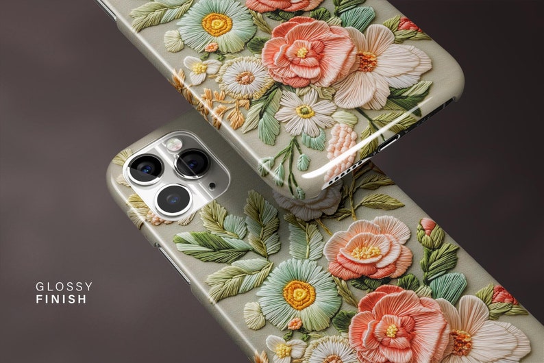 K&ouml;nnte beinhalten: Zwei Handyh&uuml;llen mit gl&auml;nzendem Finish, mit einem 3D-Blumendesign. Die H&uuml;llen zeigen eine Vielzahl von Blumen in Pfirsich-, Wei&szlig;- und Gr&uuml;nt&ouml;nen mit aufwendigen Details. Die H&uuml;llen sind hellgrau.