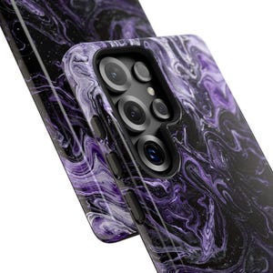May include: Two smartphone cases with a swirling marble design in shades of purple and black. The cases have a glossy finish and feature camera cutouts and side buttons. The design resembles a galaxy or nebula.