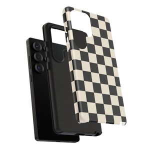 May include: A black smartphone with a black case and a separate phone case with a black and cream checkerboard pattern. The phone has three camera lenses. The phone case is slightly separated from the phone.