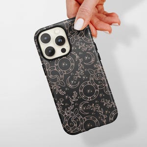 May include: Black phone case featuring a repeating pattern of snakes, crescent moons, and floral elements in a copper color. The case has a glossy finish and a camera cutout.