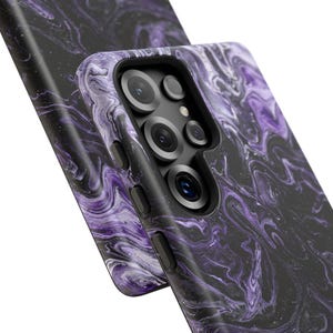 May include: Close-up of two phone cases with a swirling marble design in shades of purple and black. The cases have a glossy finish and feature camera cutouts and side buttons. The overall aesthetic is modern and stylish.