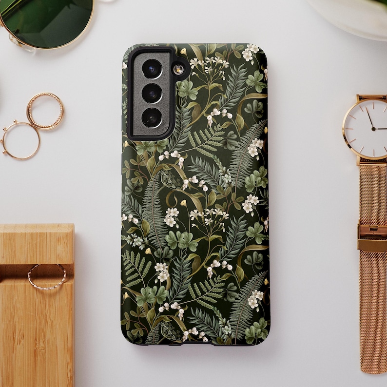 May include: A black phone case with a green floral pattern. The case has a cutout for the camera lens.
