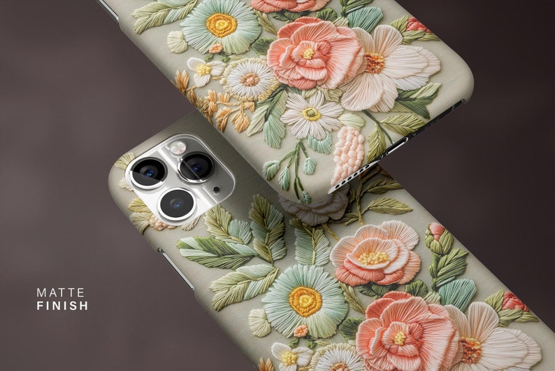 K&ouml;nnte beinhalten: Zwei Handyh&uuml;llen mit matter Oberfl&auml;che, verziert mit detaillierter Blumenstickerei in Pastellt&ouml;nen. Das Design umfasst pfirsichfarbene, wei&szlig;e und gr&uuml;ne Blumen mit aufwendigen Bl&auml;ttermustern. Der Text "MATTE FINISH" ist sichtbar.