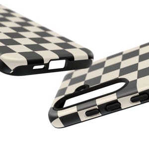 May include: Close-up of two phone cases with a black and cream checkerboard pattern. The cases have a black border and cutouts for the phone's features. The design is a classic, retro style.