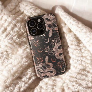 May include: Black phone case featuring a rose gold pattern of snakes, crescent moons, and stars. The case has a glossy finish and a camera cutout. The design is set against a black background.