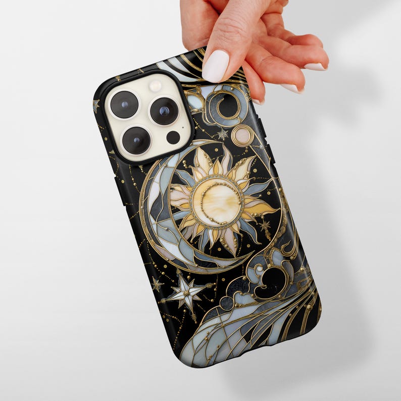 Pu&ograve; includere: Custodia per telefono nera con un design celeste con sole, luna e stelle. La custodia ha dettagli dorati e un motivo dettagliato in stile vetrata. La custodia &egrave; tenuta da una mano.