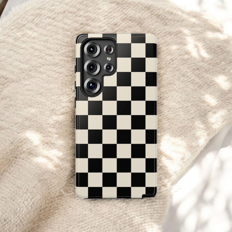 May include: A black and cream checkered phone case. The case has a glossy finish and features a grid pattern of alternating black and cream squares. The phone case has a camera module with multiple lenses.