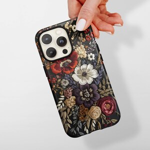K&ouml;nnte beinhalten: Schwarze Handyh&uuml;lle mit floralem Design. Die H&uuml;lle weist ein detailliertes Muster verschiedener Blumen in Rot-, Wei&szlig;-, Lila- und Gelbt&ouml;nen auf. Die Blumen sind vor einem dunklen Hintergrund angeordnet.