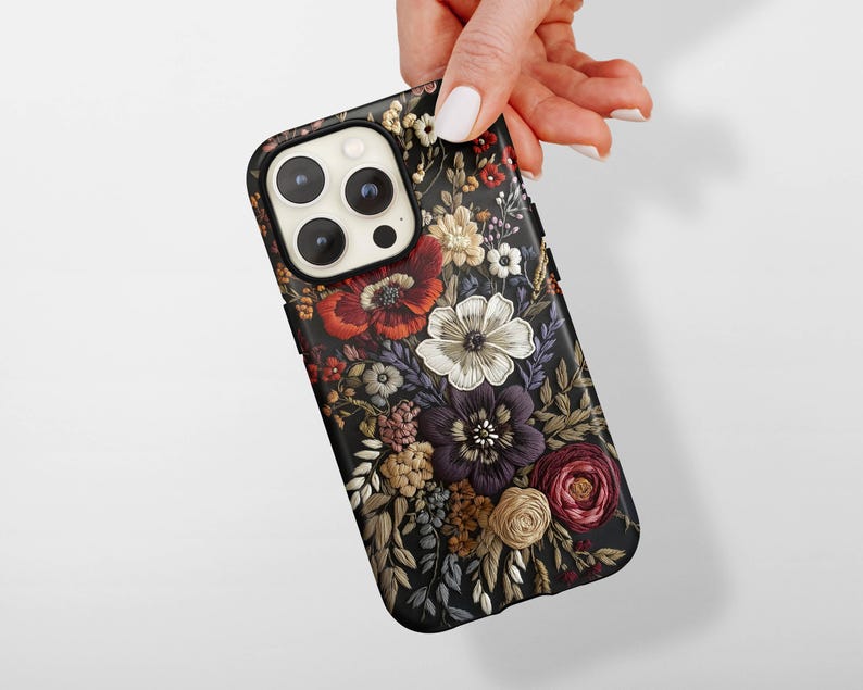 K&ouml;nnte beinhalten: Schwarze Handyh&uuml;lle mit floralem Design. Die H&uuml;lle weist ein detailliertes Muster verschiedener Blumen in Rot-, Wei&szlig;-, Lila- und Gelbt&ouml;nen auf. Die Blumen sind vor einem dunklen Hintergrund angeordnet.