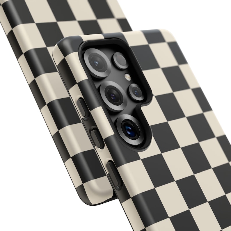 May include: Close-up of two phone cases with a black and cream checkerboard pattern. The phone cases have a sleek design and feature multiple camera lenses. The cases are angled, showcasing the pattern and design.