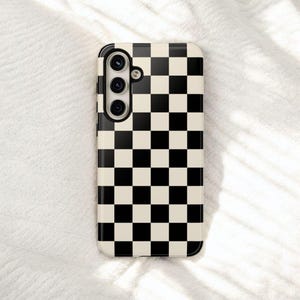 May include: A phone case with a black and cream checkerboard pattern. The case has a camera module with three lenses and a flash. The case is rectangular with rounded corners.