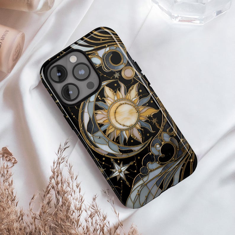 Pu&ograve; includere: Custodia per telefono nera con un design celeste con sole, luna e stelle in oro, giallo e grigio. La custodia ha una finitura lucida e un bordo nero. Il design ricorda le vetrate.