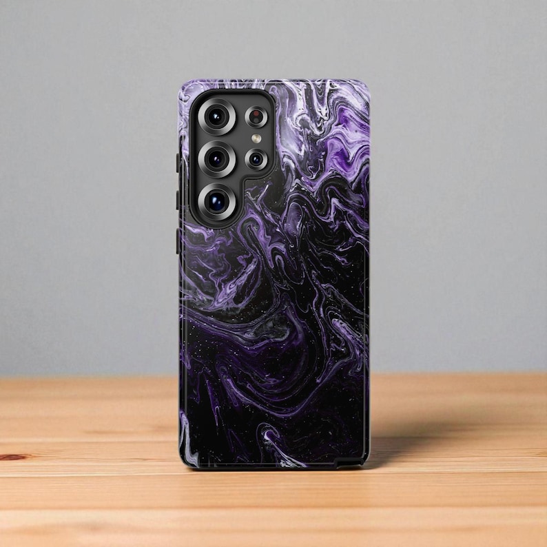 May include: A smartphone case with a swirling purple and black marble design. The case has a glossy finish and a camera cutout with multiple lenses. The case is on a wooden surface.