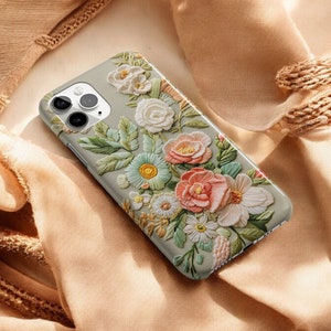 iPhone case with an intricate floral embroidery. lying on top of a soft fabric background with delicate flowers and leaves. The case features focus stacking, cottagecore aesthetics, vintage style