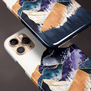 May include: Two smartphone cases with a glossy finish. The cases feature a design with gold, blue, and white abstract shapes. One case is white, and the other is dark blue with a forest scene.