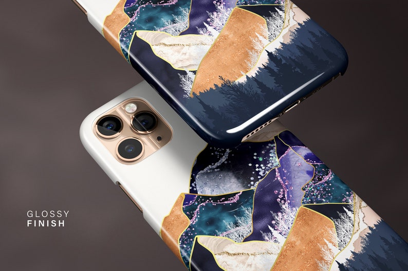May include: Two smartphone cases with a glossy finish. The cases feature a design with gold, blue, and white abstract shapes. One case is white, and the other is dark blue with a forest scene.