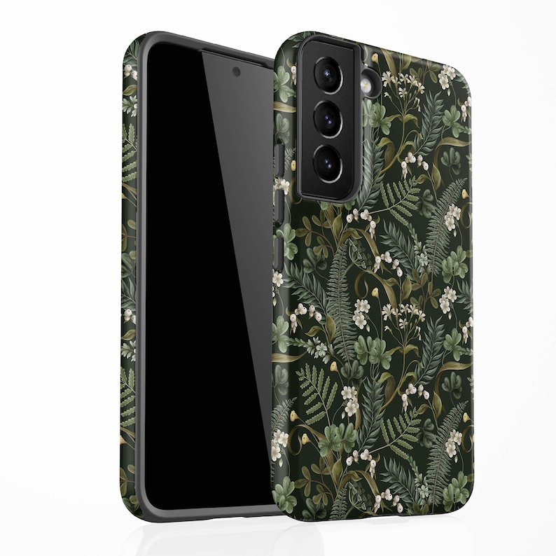 May include: A black phone case with a floral pattern featuring green leaves, white flowers, and gold accents. The case has a cutout for the camera lens.