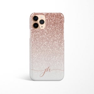 May include: Rose gold glitter iPhone case with a gradient effect, transitioning from a sparkling top to a softer, lighter bottom. Features a delicate cursive "jh" monogram. The case has a camera module with three lenses.