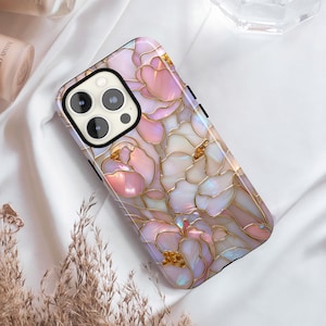Op de afbeelding: Een telefoonhoesje met een bloemenpatroon in roze, wit en goud. De hoes heeft een glanzende afwerking en een zwarte rand. Het ontwerp lijkt op glas-in-lood, met gedetailleerde lijnen en een parelmoer effect.