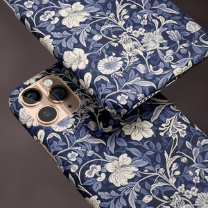 May include: Two phone cases with a floral pattern in navy blue, light blue, and white. The cases have a matte finish. The phone case has a gold camera lens.