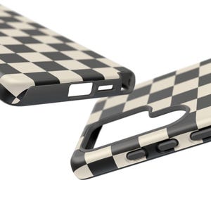 May include: Two black and cream checkered phone cases. The cases have a black border and cutouts for the camera, buttons, and charging port. The checkered pattern is a classic design.