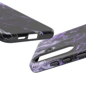 May include: Two black phone cases with a swirling purple and white marble design. The cases have a matte finish and feature cutouts for the camera, buttons, and charging port. The cases are shown at an angle against a white background.