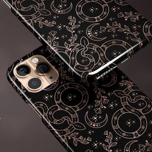 以下が含まれることがあります： 金色の蛇、月、星のパターンが施された黒い携帯電話ケース。ケースは光沢のある仕上げです。