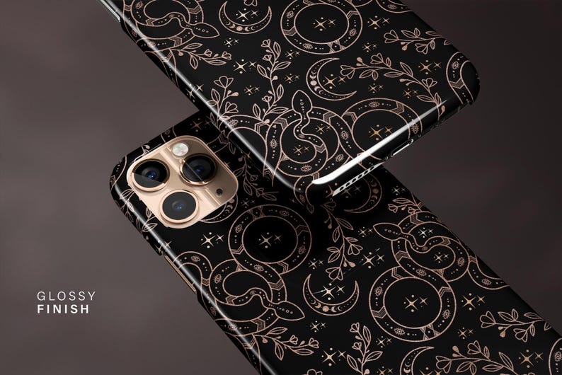 May include: Two black phone cases with a glossy finish. The cases feature a repeating pattern of snakes, crescent moons, stars, and floral elements in a copper color. The phone cases are angled, showing the camera and the design.