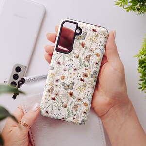 May include: A white phone case with a floral pattern featuring butterflies and small flowers in shades of brown, pink, and green.