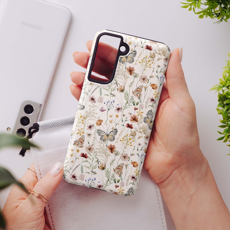 May include: A white phone case with a floral pattern featuring butterflies and small flowers in shades of brown, pink, and green.