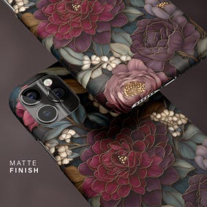 Op de afbeelding: Twee telefoonhoesjes met een bloemenpatroon. De hoesjes tonen grote, gestileerde bloemen in tinten bordeauxrood, paars en goud, tegen een donkere achtergrond met groene en blauwe bladeren. De tekst "MATTE FINISH" is zichtbaar op een hoesje.