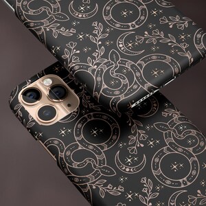 May include: Black phone cases with a matte finish, featuring a repeating pattern of snakes, crescent moons, stars, and floral elements in a rose gold color. The text "MATTE FINISH" is visible.