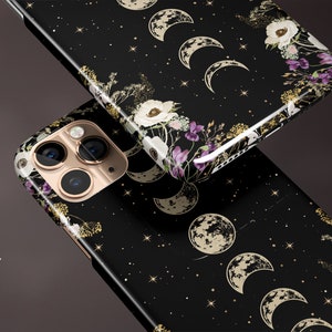 May include: Black phone case with a glossy finish, featuring a celestial design. The case displays phases of the moon, stars, and floral accents in white, gold, and purple. The phone case is shown at an angle.