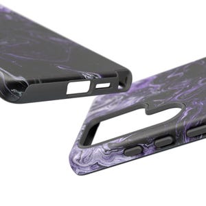 May include: Two black phone cases with a purple and white marbled design. The cases have a sleek, modern design with cutouts for the camera and buttons. The cases are made of a durable material and offer protection for the phone.