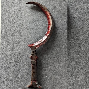 Könnte beinhalten: Eine gebogene, halbmondförmige Metallklinge mit einem blutroten Farbton am Rand. Der Griff ist dunkelbraun mit strukturiertem Griff. Die Waffe hat ein dekoratives, spitzes Design an der Basis der Klinge und des Griffs.
